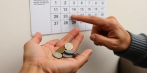Elderly person holding coins, looking at calendar.